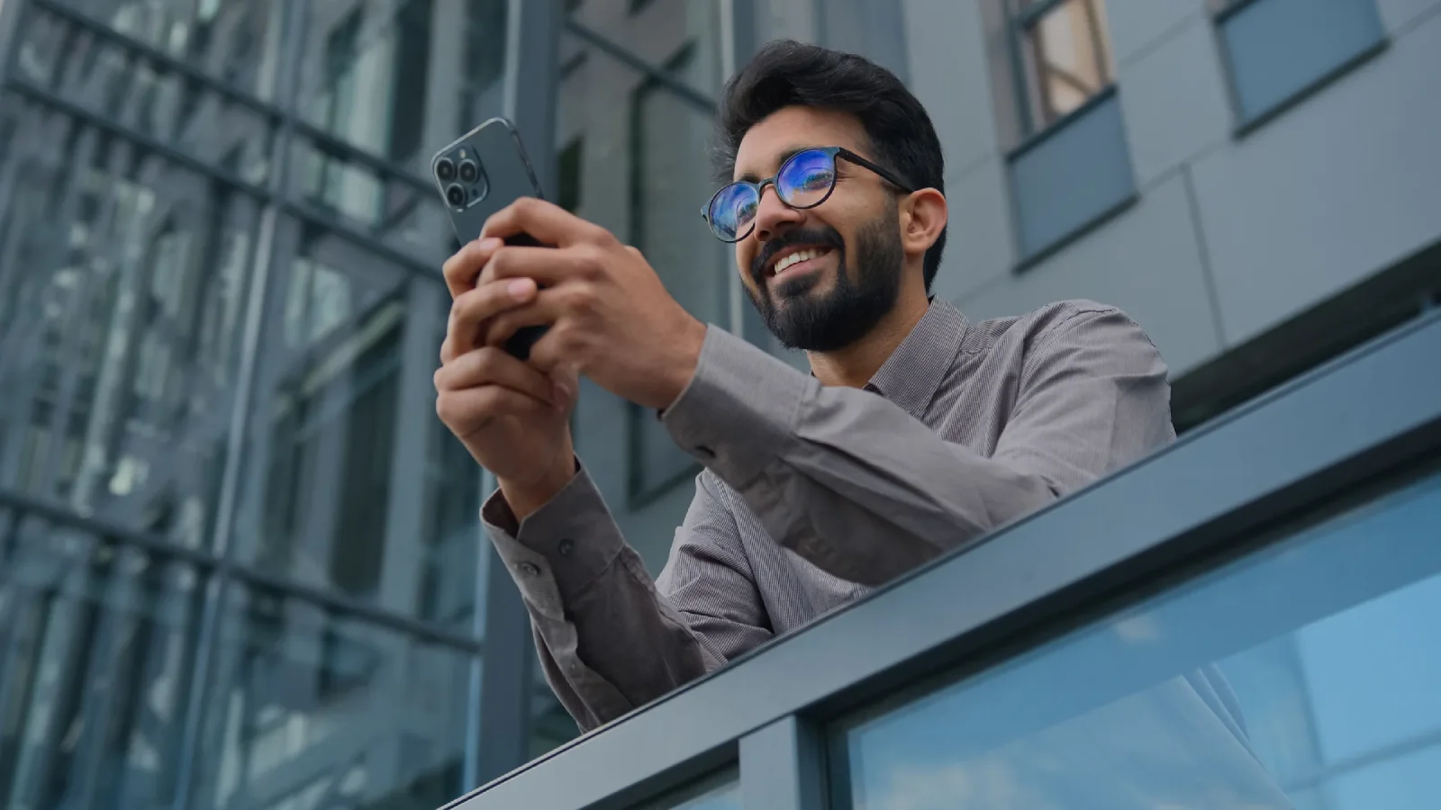 Male with glasses texting over a building
