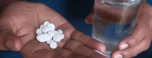 person holding medication pills on hand and a glass of water